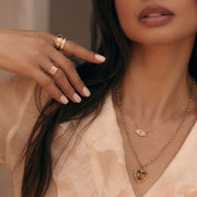 Woman wearing gold jewelry including a personalized necklace, ring, and bracelet against a neutral background.